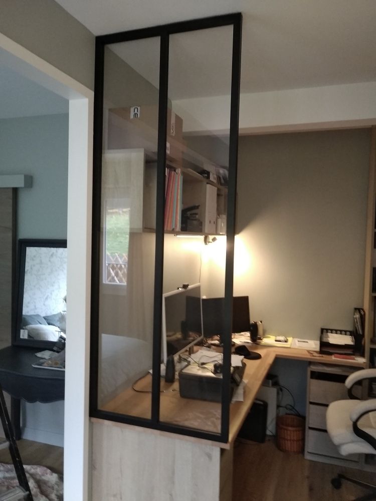 Une cloison vitrée à cadre noir sépare un espace de travail à domicile d'une pièce adjacente.