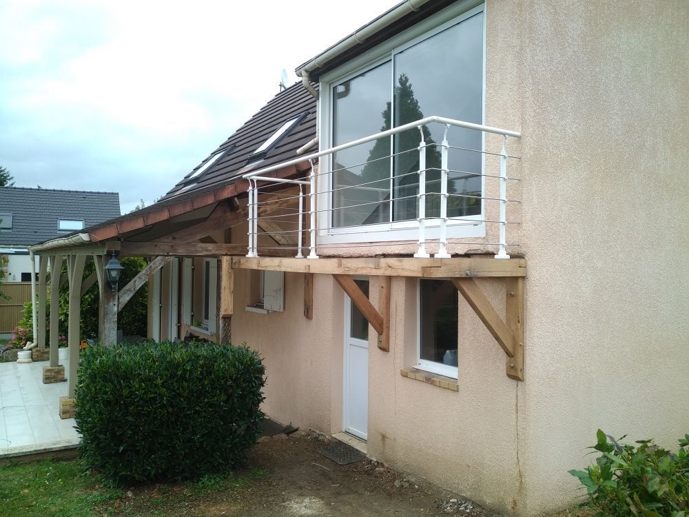 Vue extérieure d'une maison présentant un balcon en bois soutenu par des consoles inclinées, avec une rambarde blanche à l'extérieur d'une fenêtre.