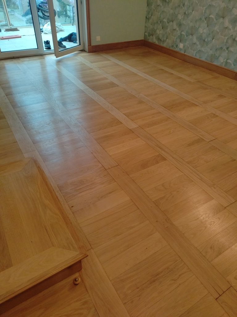 Un parquet clair à motifs quadrillés dans une pièce offrant une vue partielle sur une porte vitrée.