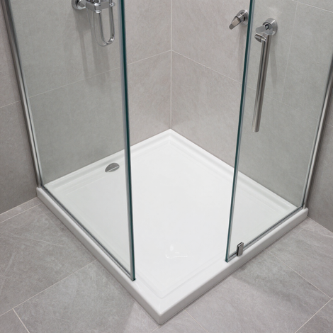 Ducha esquinera a ras de suelo con puertas de cristal, plato blanco y paredes y suelo de azulejos grises.