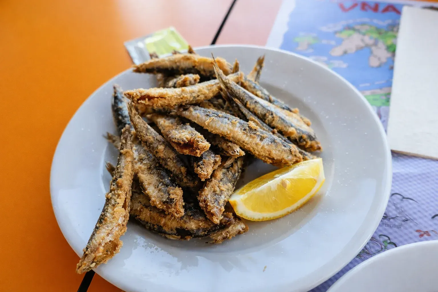 Plato de pescado pequeño frito con rodaja de limón sobre una mesa naranja.
