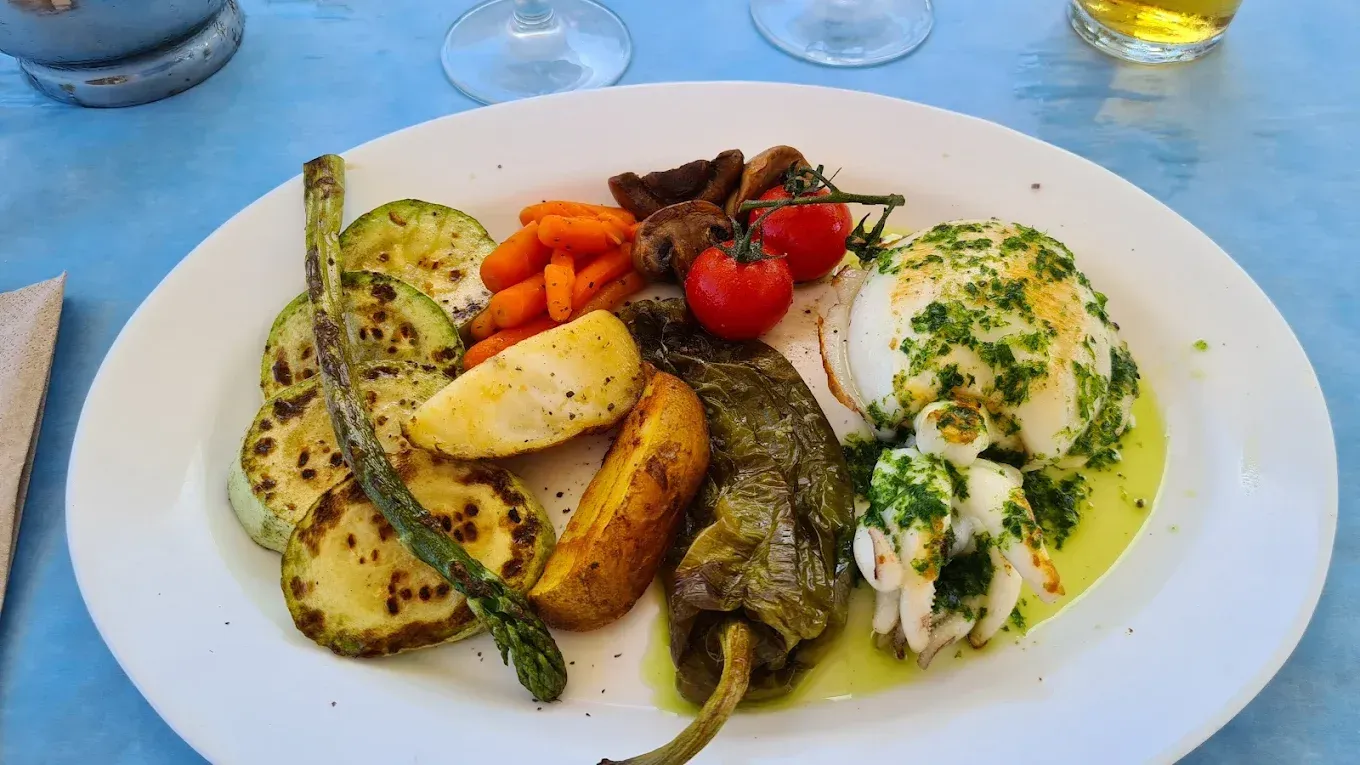 Verduras y mariscos a la parrilla en un plato blanco, sobre una mesa azul.