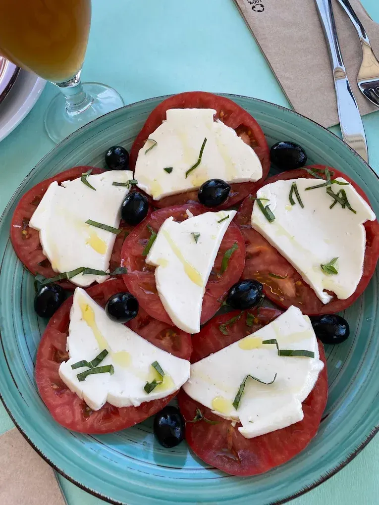 Ensalada de tomate y mozzarella con aceitunas y hierbas en un plato verde azulado.