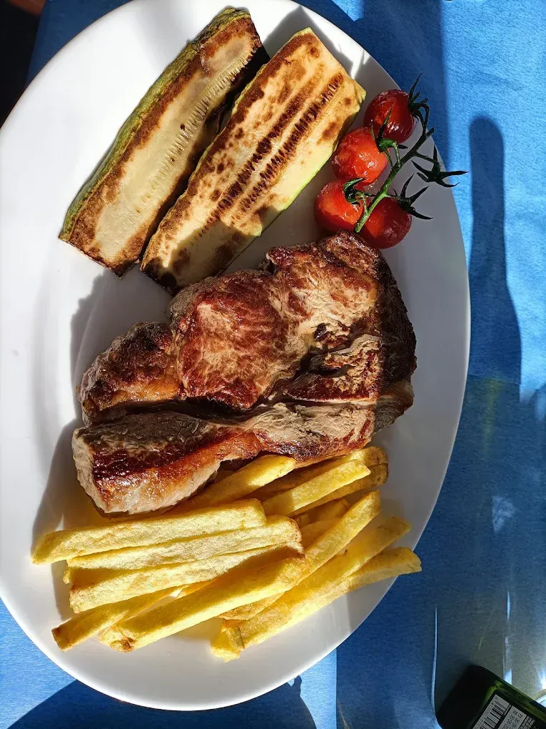 Bistec a la parrilla con patatas fritas, calabacín a la parrilla y tomates cherry en un plato blanco.