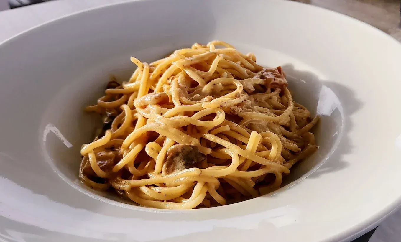 Espaguetis a la carbonara en un tazón blanco, primer plano. Pasta bañada en salsa y cubierta con queso rallado.