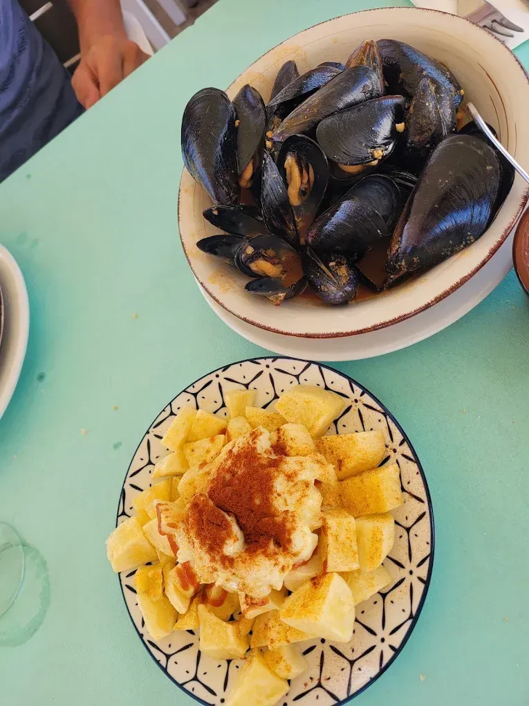 Cuenco de mejillones y patatas con pimentón sobre una mesa turquesa.