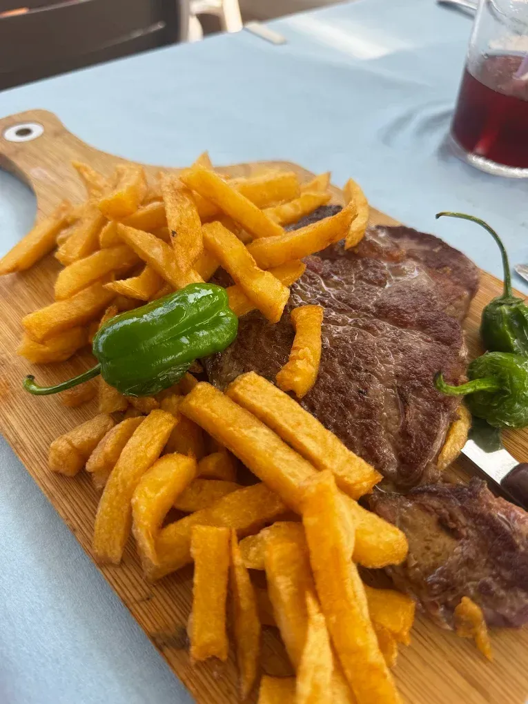 Bistec con patatas fritas y pimientos sobre tabla de madera.