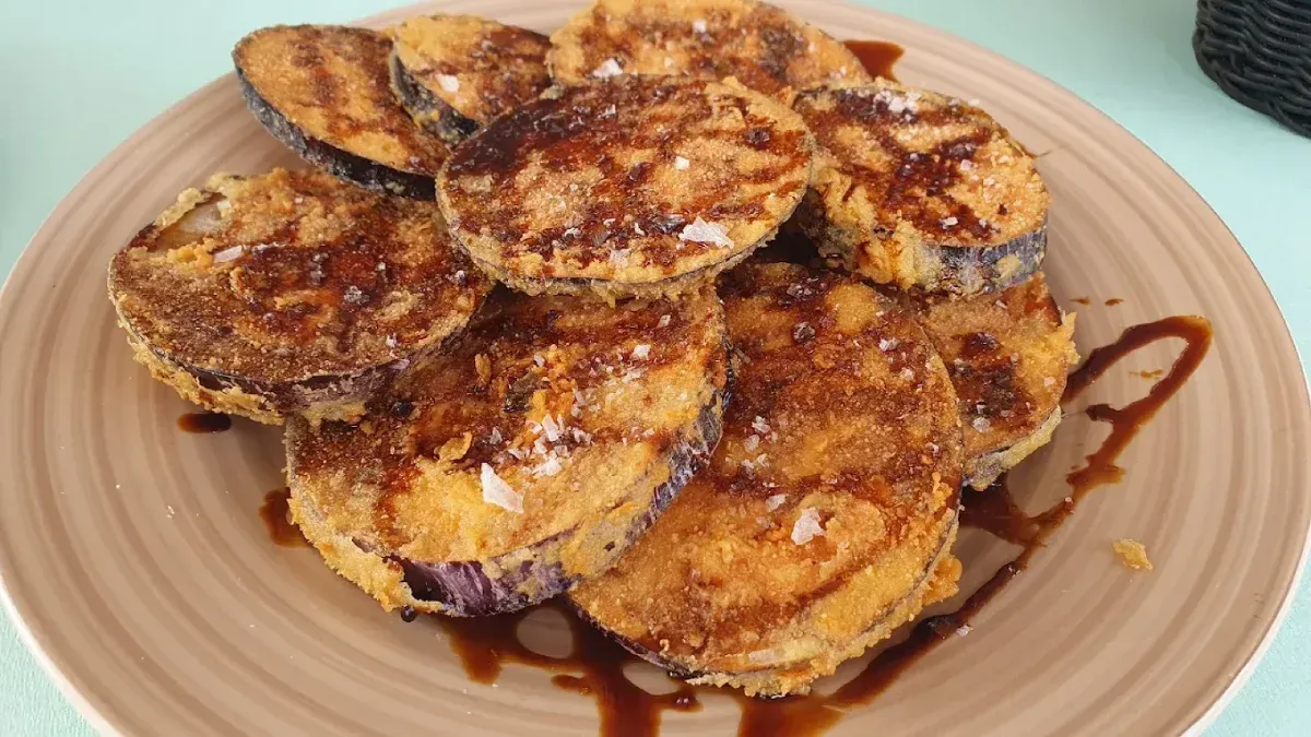 Plato de rodajas de berenjena fritas rociadas con salsa y espolvoreadas con sal gruesa.