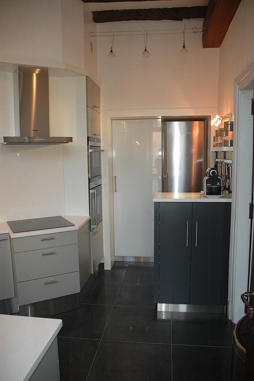 Cuisine moderne étroite avec sol carrelé foncé, placards blancs, appareils électroménagers en inox et îlot central noir.