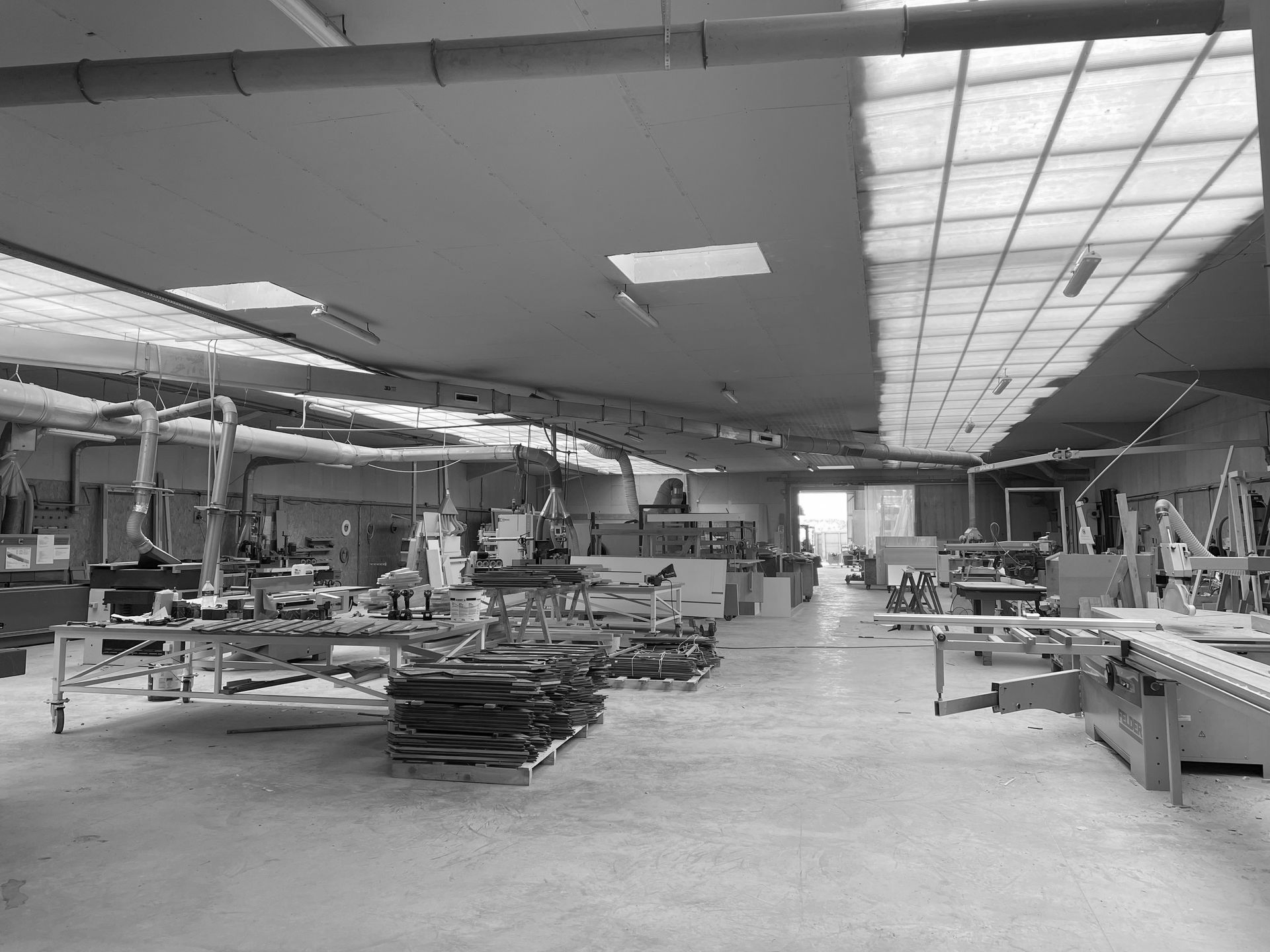 Atelier spacieux avec établis, matériaux empilés et puits de lumière au plafond.