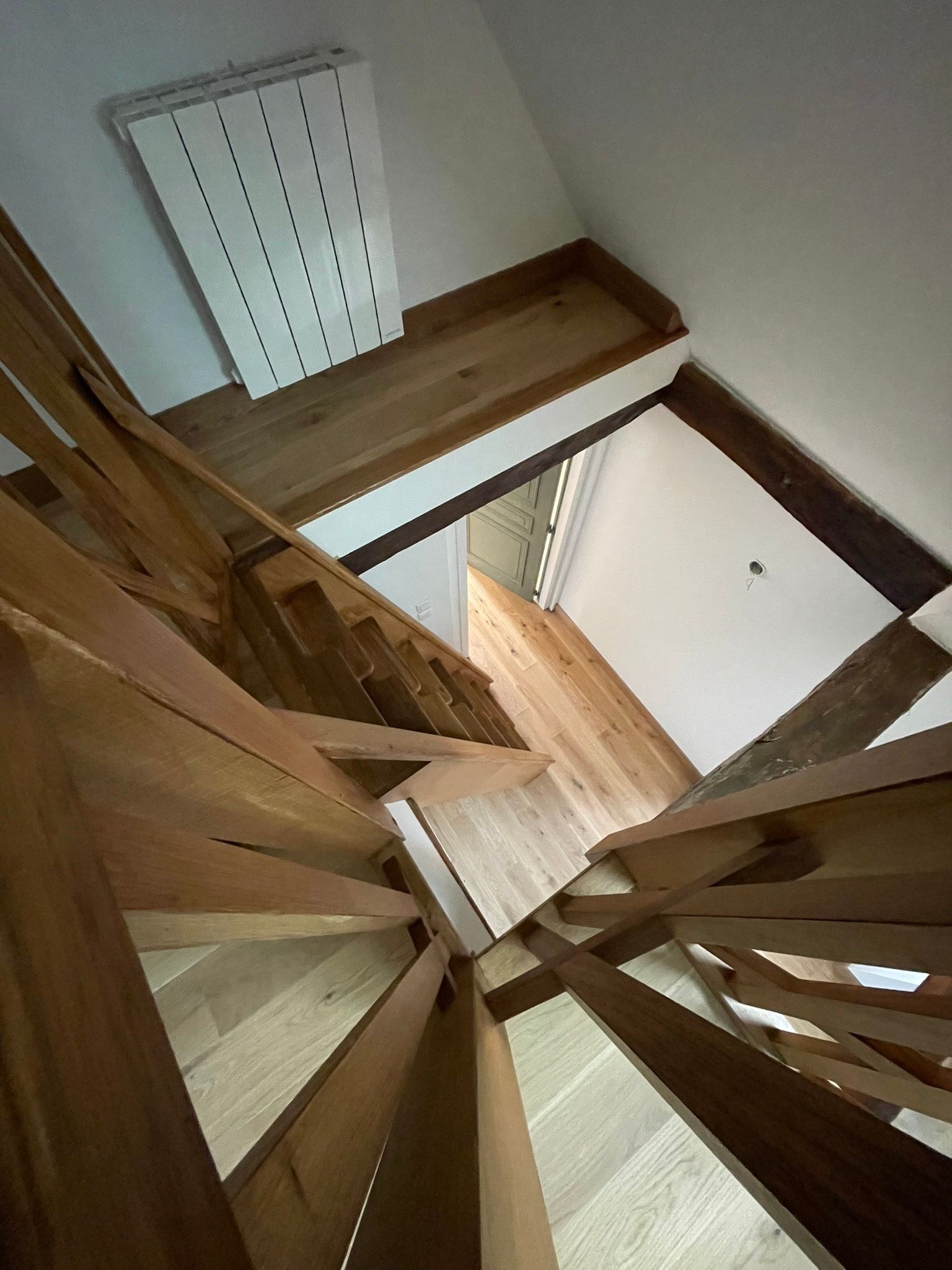 Vue de dessus d'un escalier en bois avec rampe et petit palier dans un intérieur blanc.