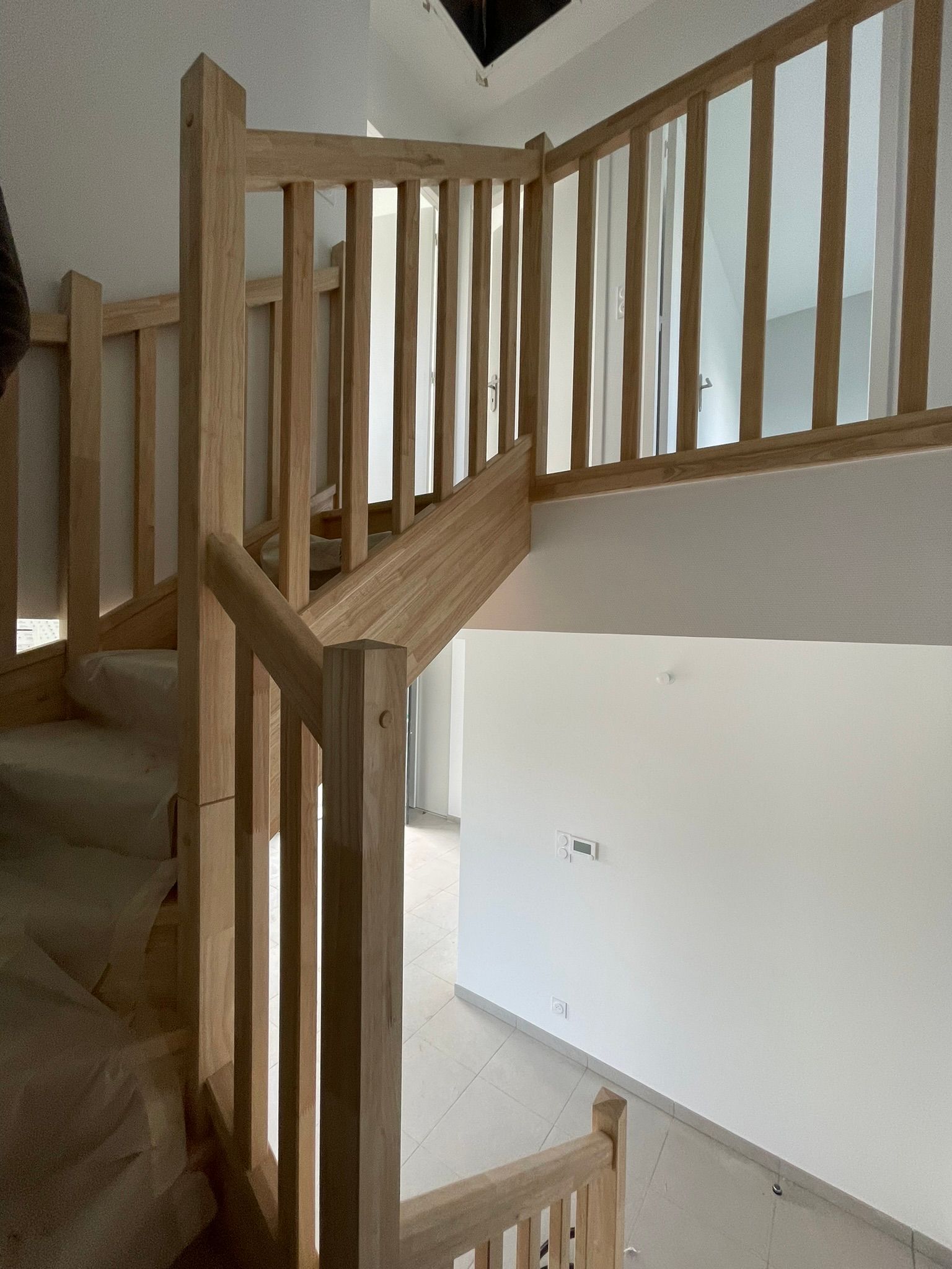Escalier en bois avec rampe et murs blancs dans un intérieur de maison.