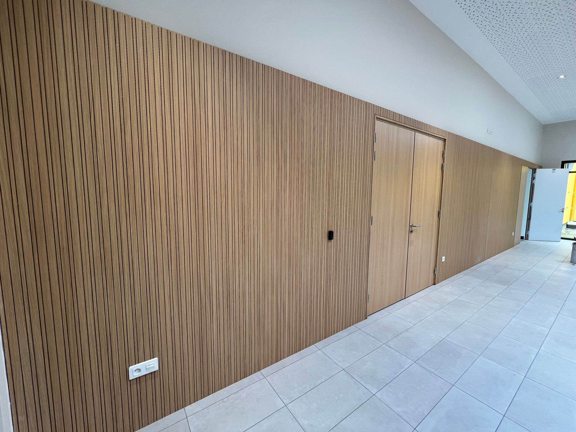 Mur lambrissé à côté d'un sol carrelé dans un couloir.