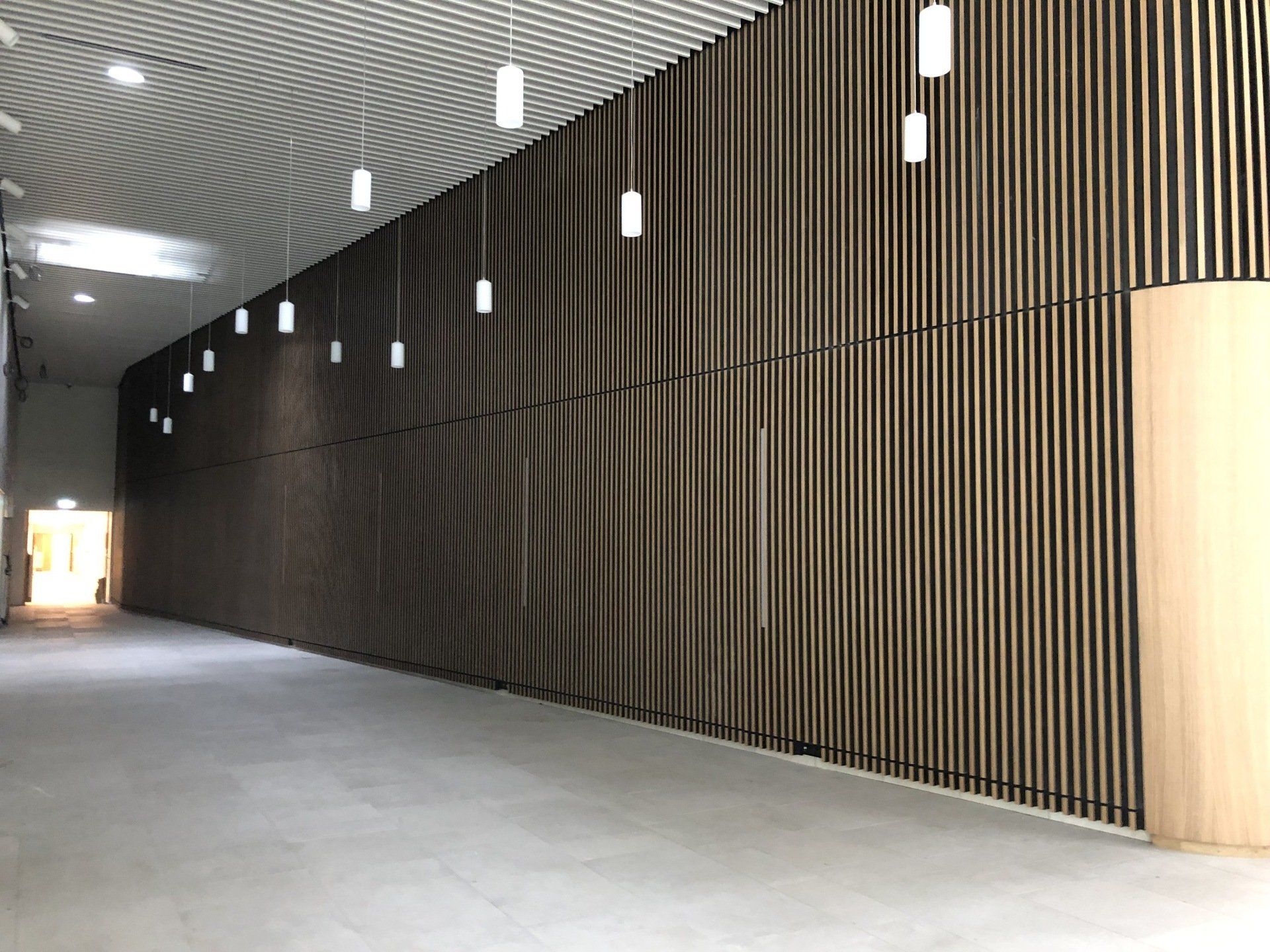 Couloir vide avec murs en revêtement bois et luminaires suspendus.
