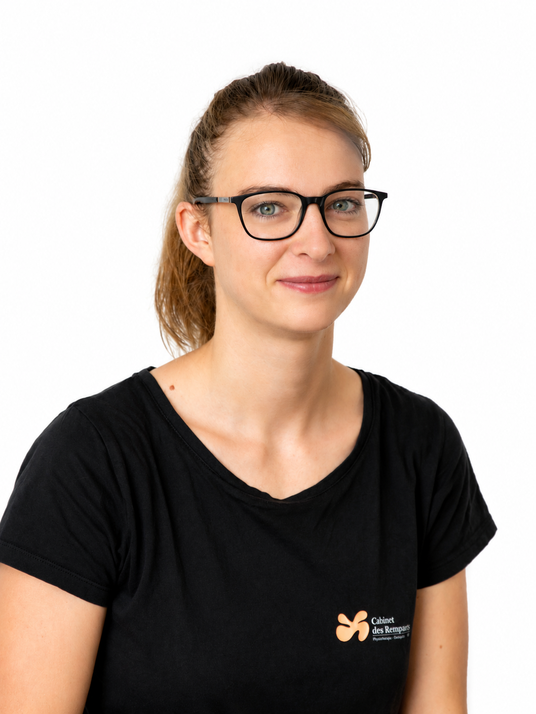 Une femme portant des lunettes et une queue de cheval sourit, vêtue d'un t-shirt noir.