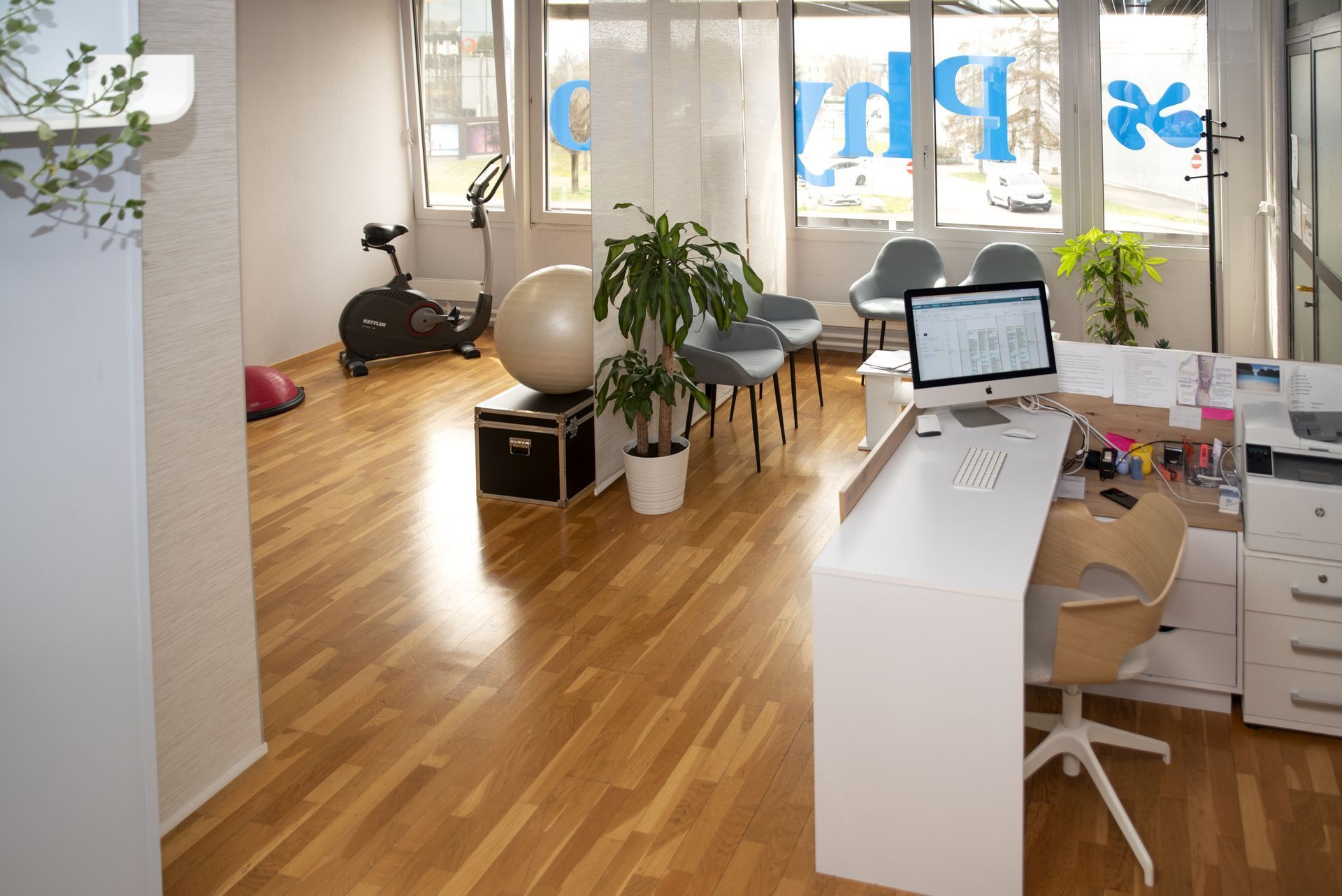Intérieur d'une clinique de physiothérapie avec comptoir d'accueil, équipements d'exercice et salle d'attente avec chaises.
