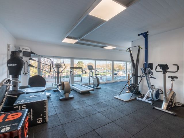 Salle de sport équipée de divers appareils de musculation, notamment des tapis de course, des vélos et un sac de frappe.