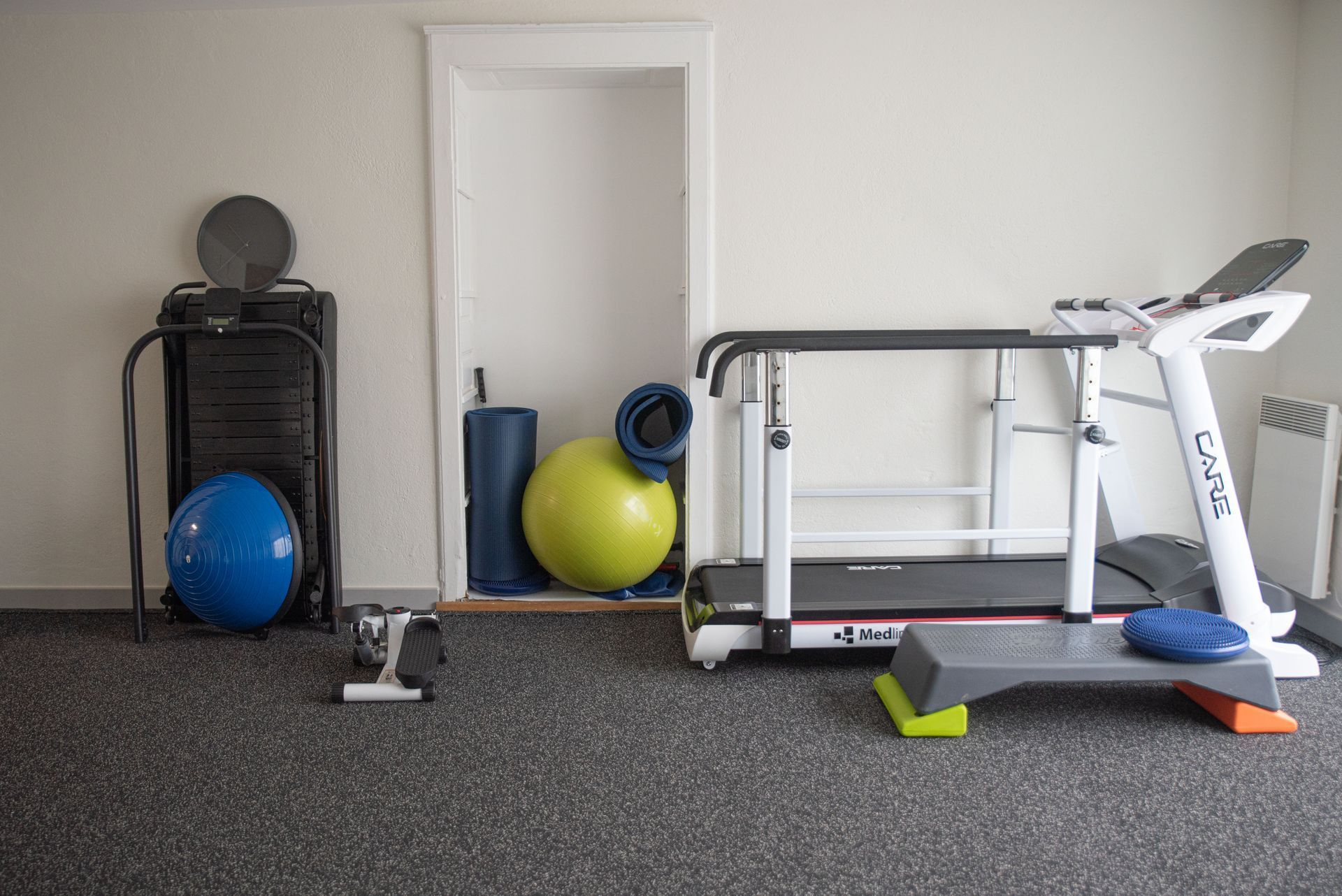 Salle de sport à domicile avec tapis roulant, appareils de musculation et ballons bleus et jaunes.