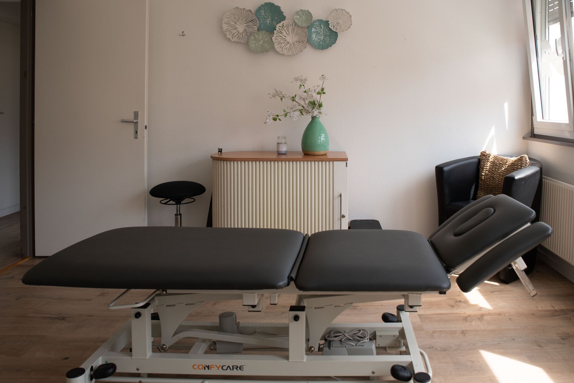 Table de massage dans une pièce baignée de lumière, avec des œuvres d'art murales décoratives.