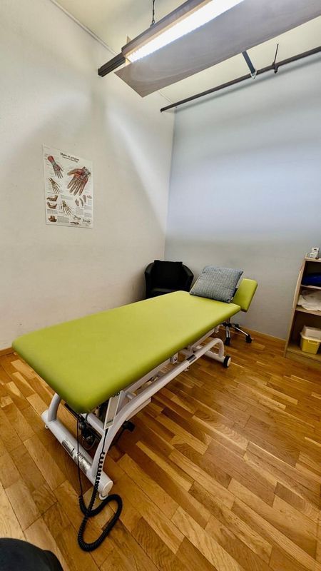 Une salle d'examen médical avec une table verte, un schéma anatomique et un sol en bois.