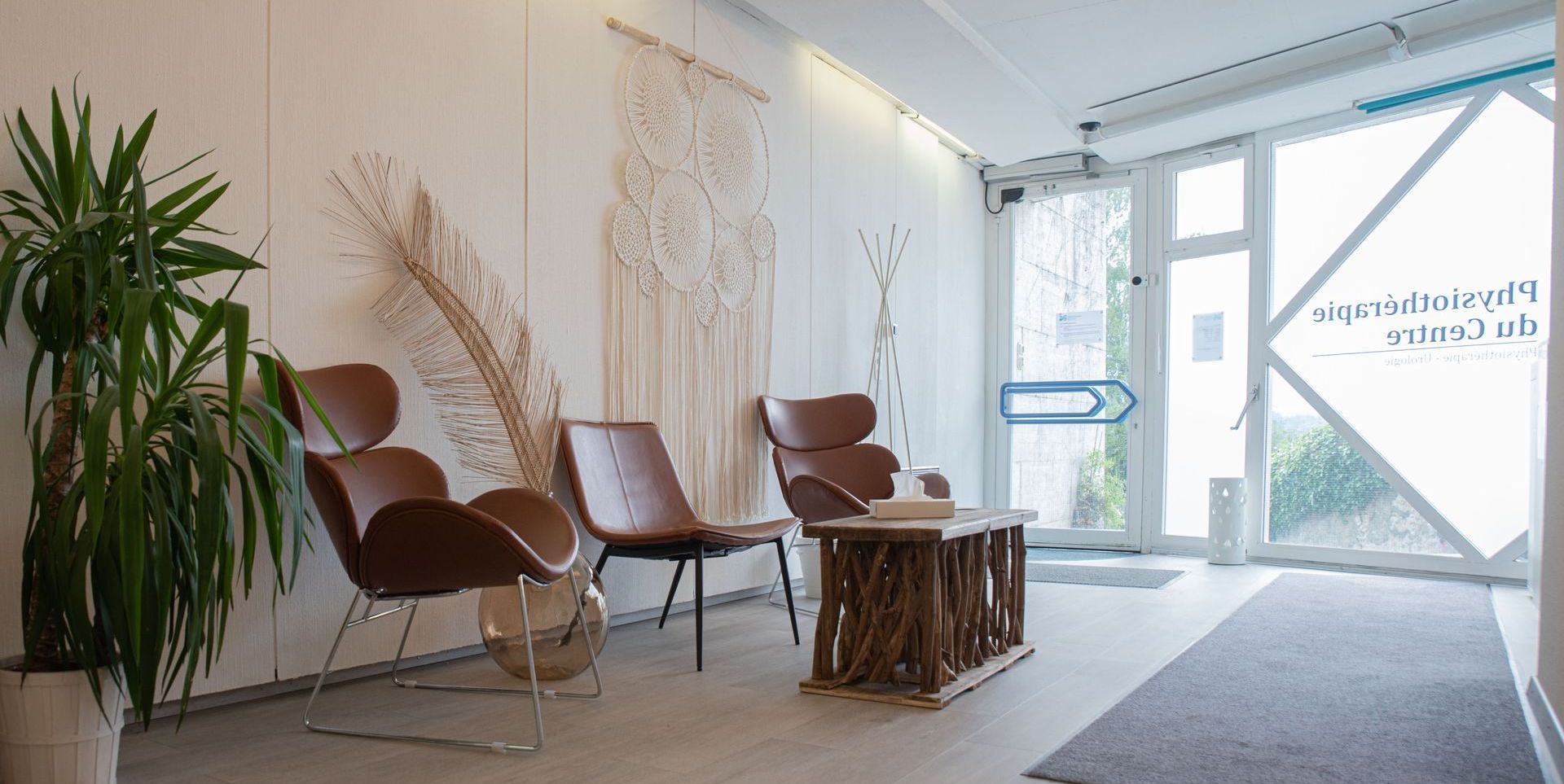 Salle d'attente avec chaises, table et plantes près d'une porte vitrée.