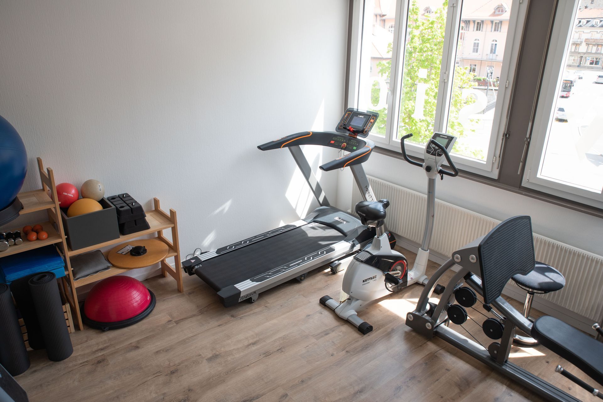 Salle de sport avec tapis roulant, vélo d'appartement et divers équipements de fitness près d'une fenêtre.