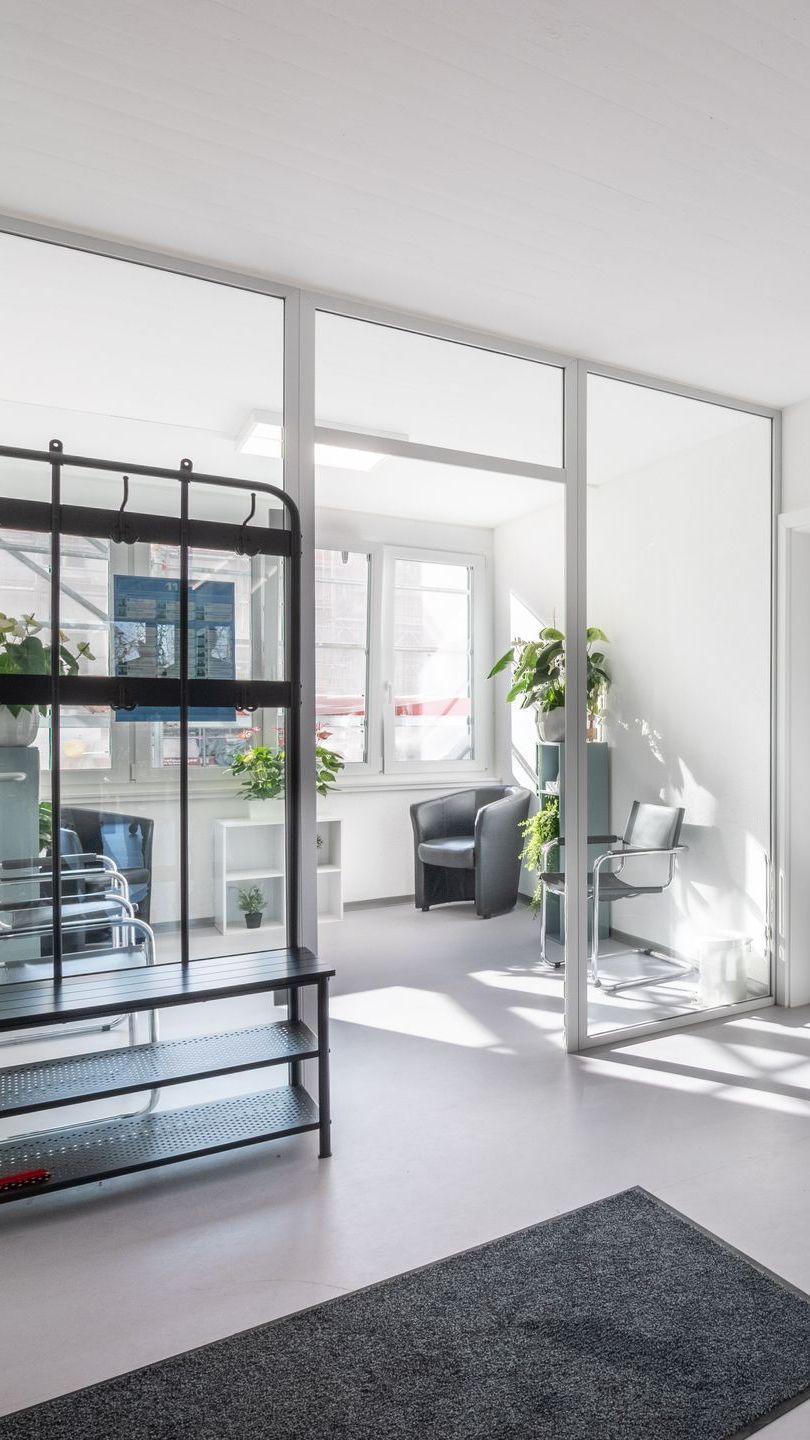 Espace de bureaux moderne avec cloisons vitrées, plantes et étagères en métal noir.