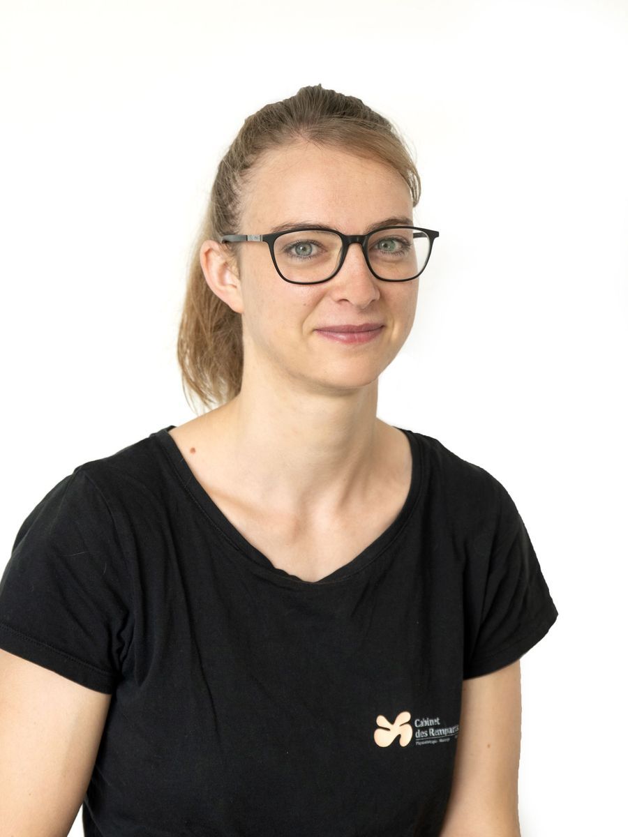 Une femme portant des lunettes et une queue de cheval sourit, vêtue d'un t-shirt noir.