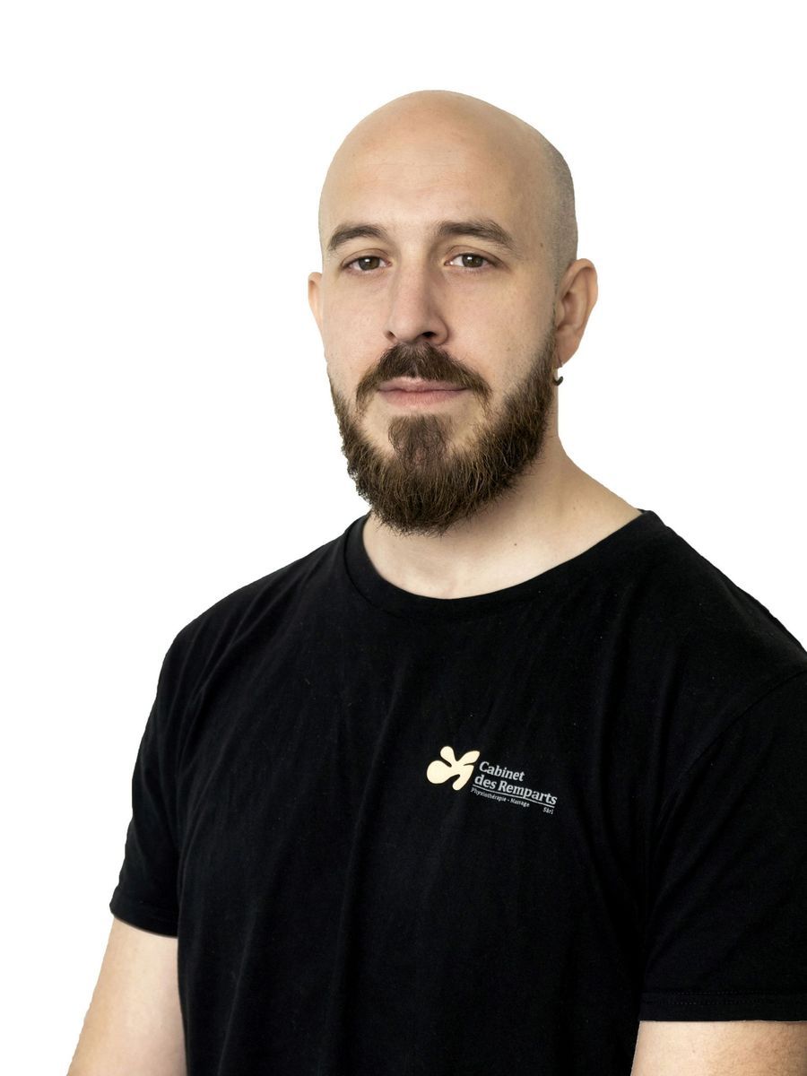 Un homme chauve à la barbe fournie, portant un t-shirt noir, regarde droit dans l'objectif.