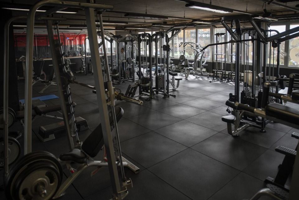 Intérieur de salle de sport avec diverses machines et équipements de musculation, sol noir et plafond apparent.