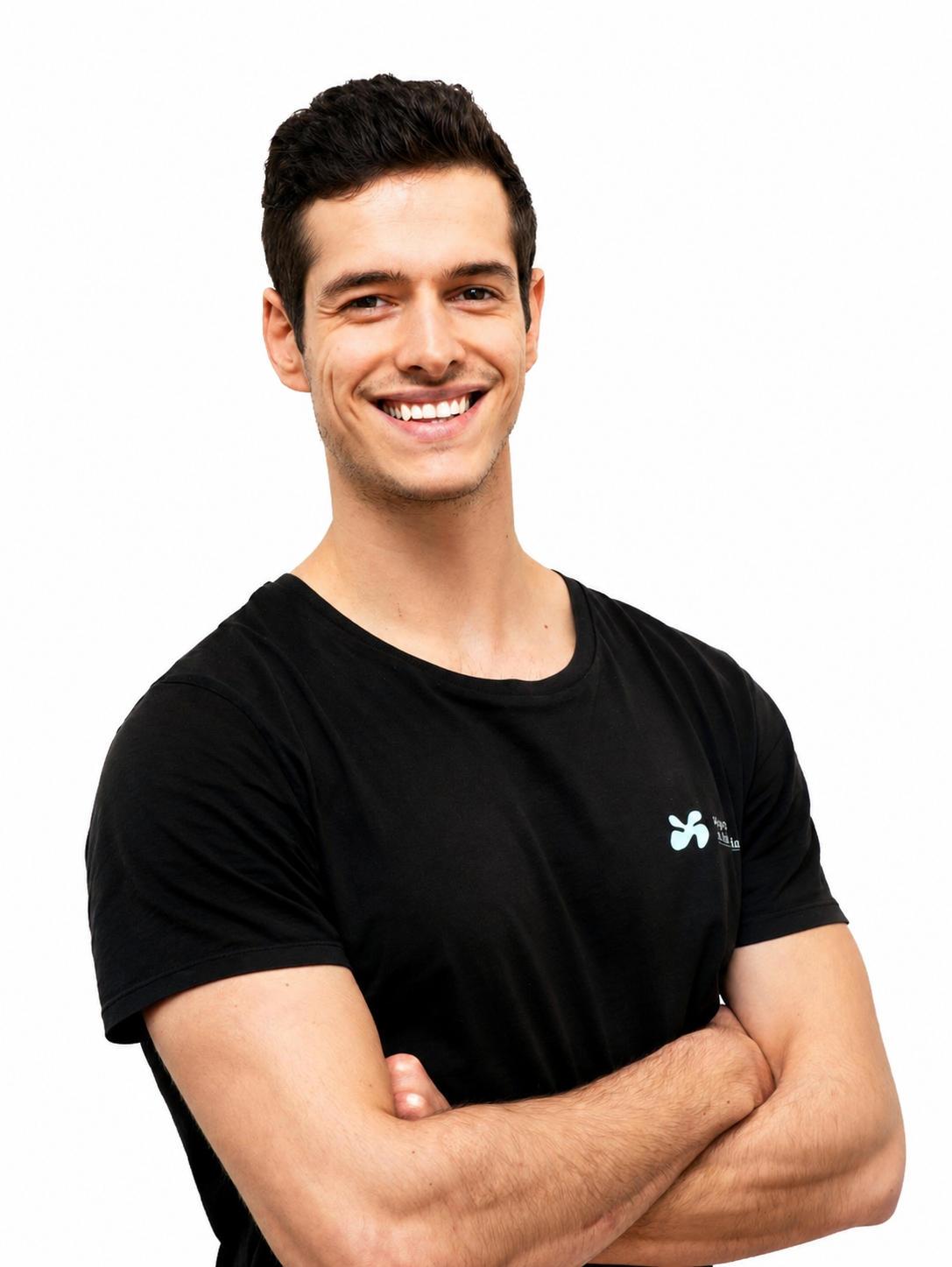Un homme, les bras croisés, souriant, vêtu d'un t-shirt noir, se tient devant un mur blanc.