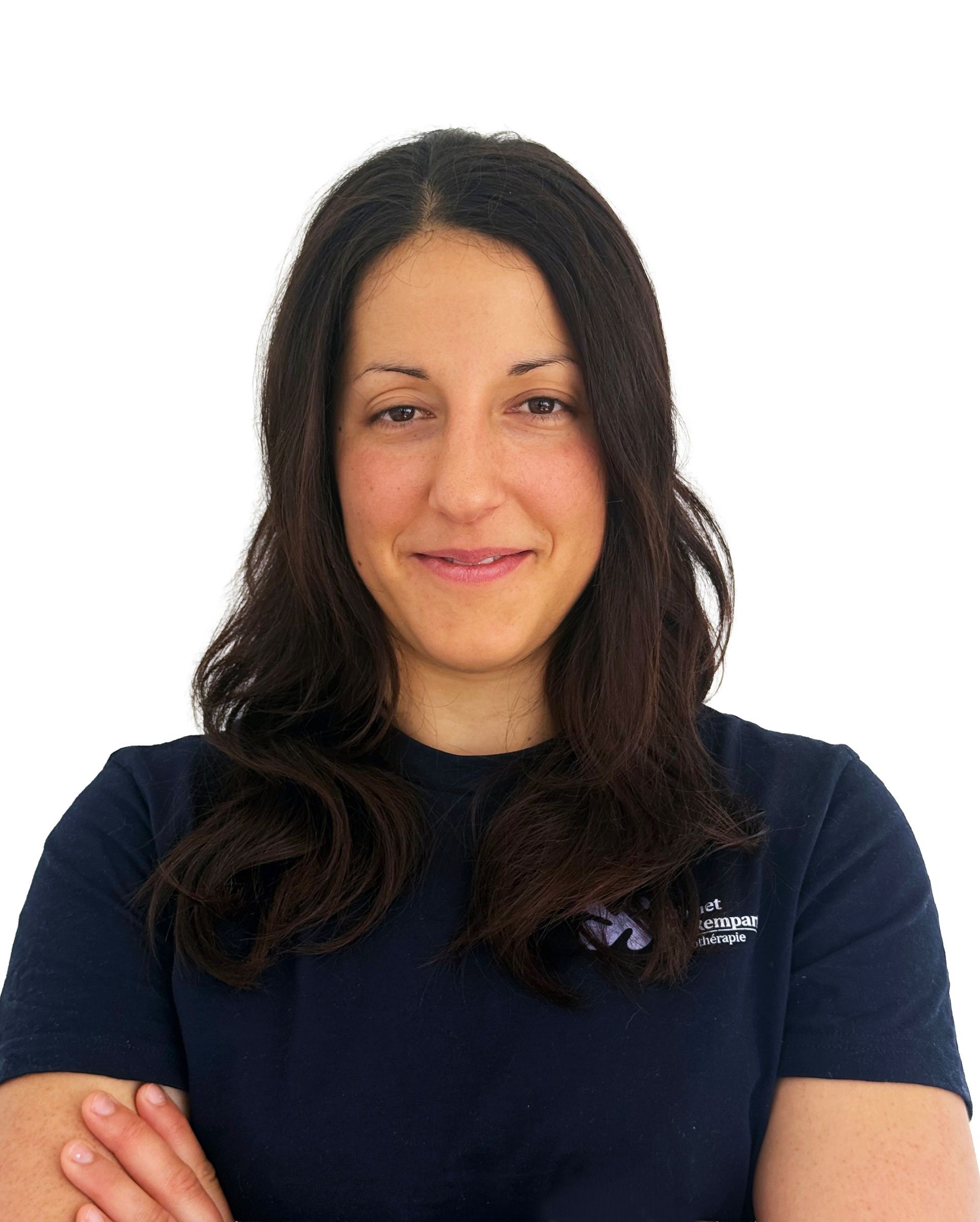 Femme aux longs cheveux noirs, vêtue d'une chemise bleu marine, debout sur fond blanc, les bras croisés et un léger sourire aux lèvres.