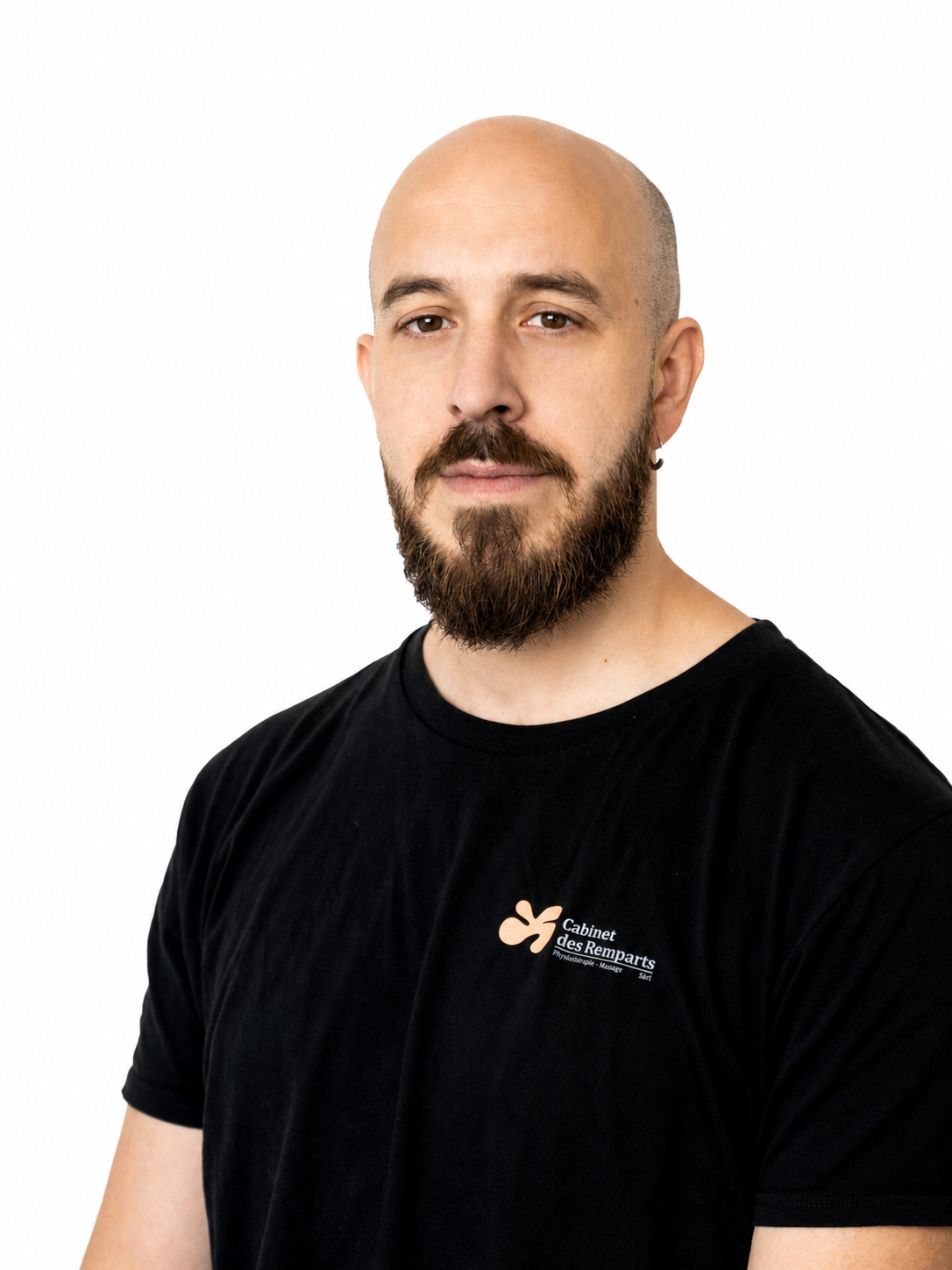 Un homme chauve à la barbe fournie, portant un t-shirt noir, regarde droit dans l'objectif.