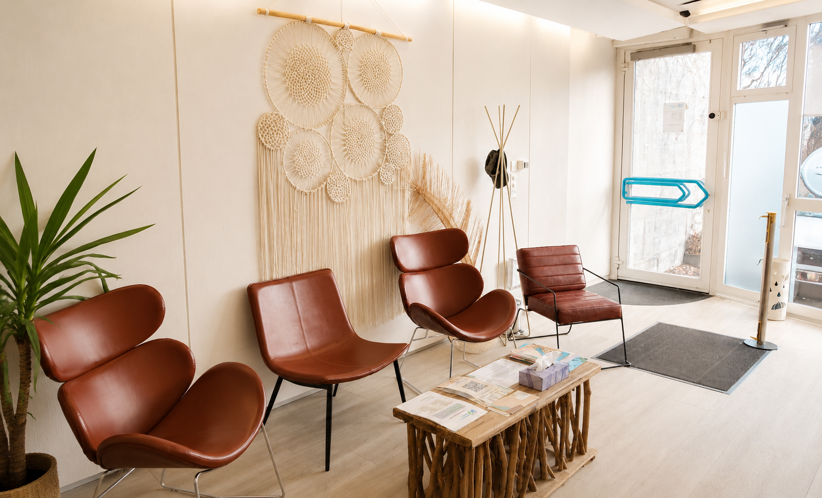 Salle d'attente moderne avec chaises marron, décoration murale tissée, une plante et une petite table basse en bois