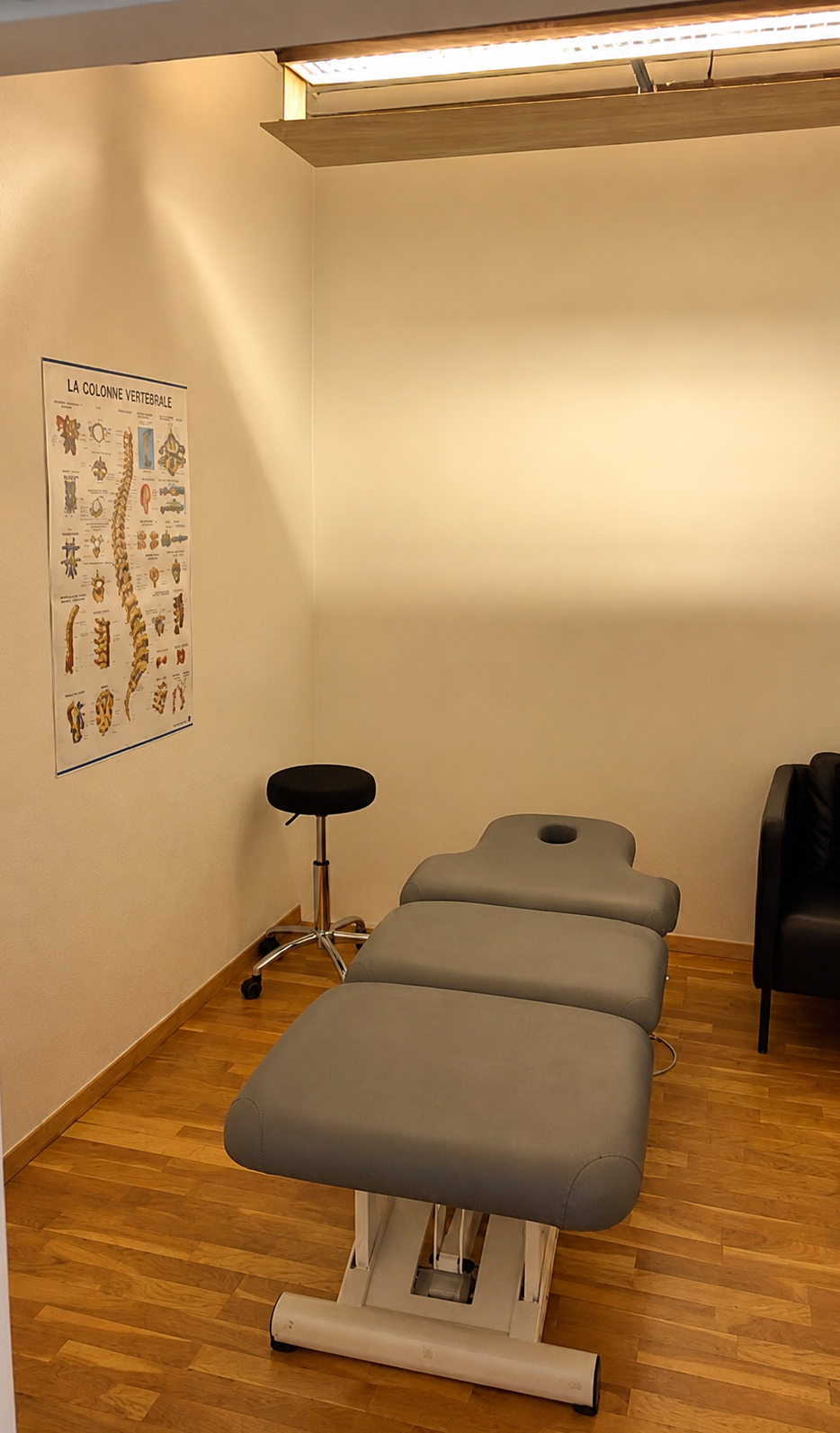 Table de traitement chiropratique dans une petite salle d'examen avec un tableau mural et un tabouret.