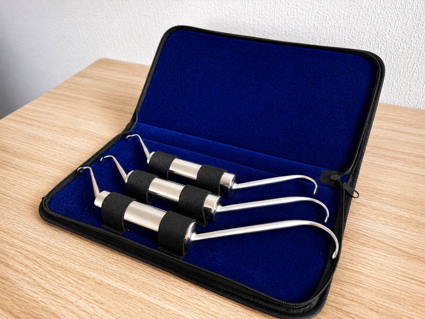 Un coffret bleu ouvert sur une table en bois, contenant trois outils à câbles noirs et argentés avec des cordons blancs.