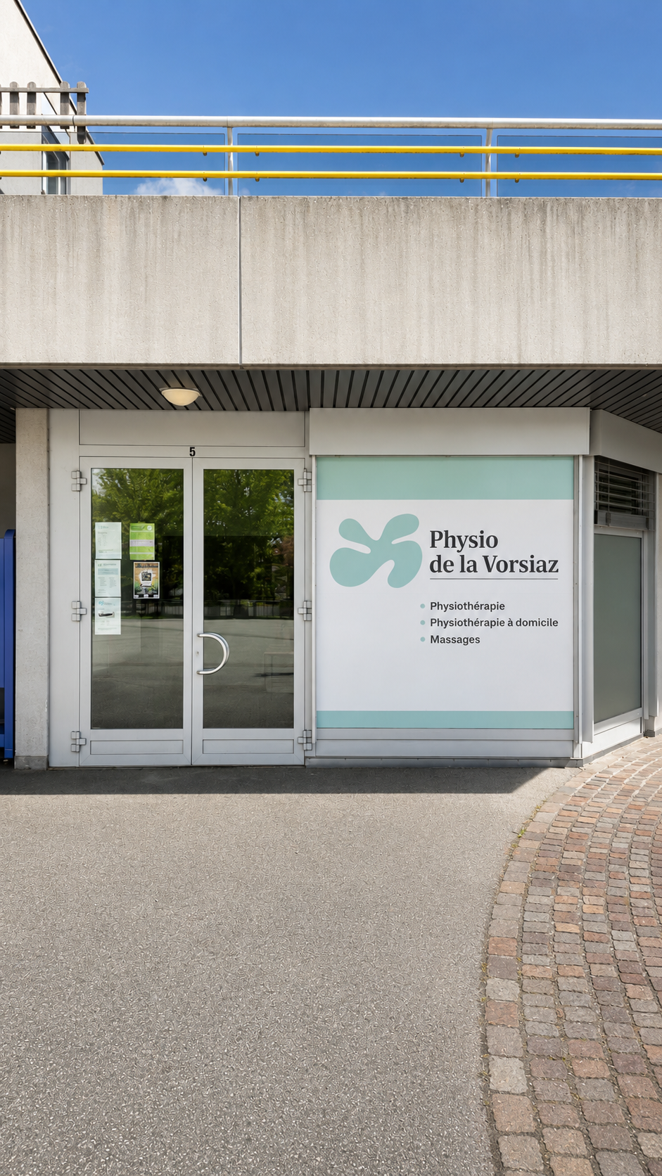 Entrée d'un immeuble avec des portes vitrées et une enseigne indiquant « Hydro La Voisier » à côté d'une façade en béton.