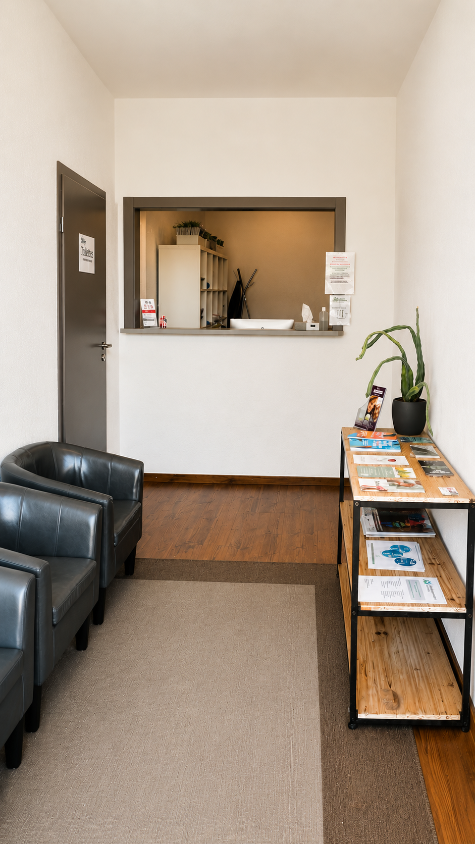 Petite salle d'attente avec chaises noires, guichet d'accueil et présentoir à brochures sur la droite.