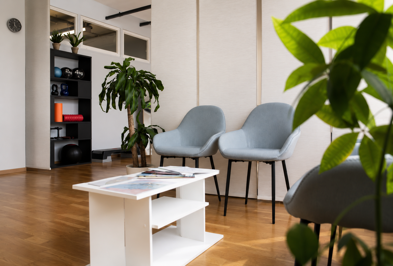 Salon moderne avec des chaises grises, une table basse blanche, un parquet et une plante en pot au premier plan.