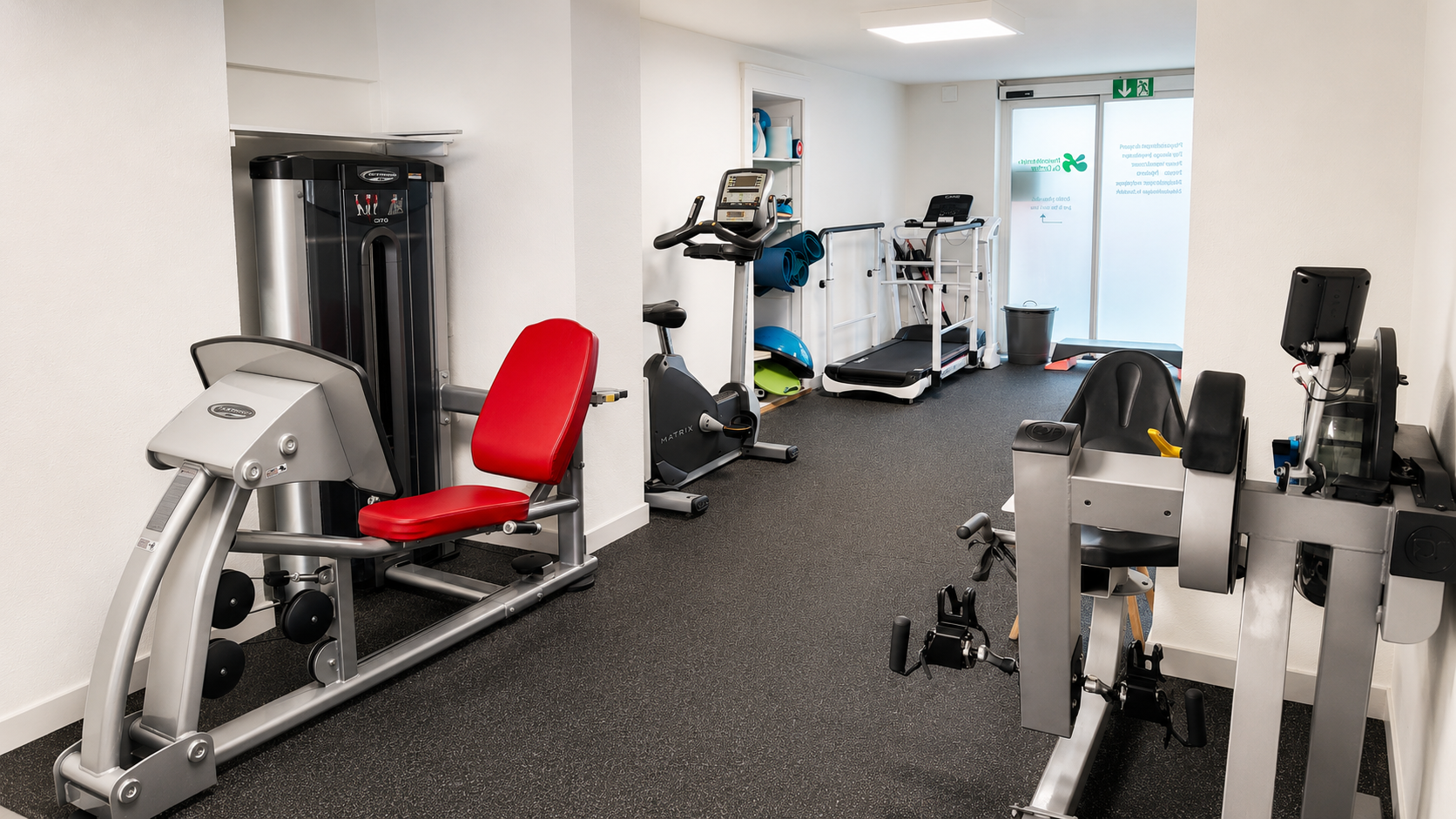 Salle de sport compacte avec appareils de musculation et de cardio-training rouges et gris près d'une porte