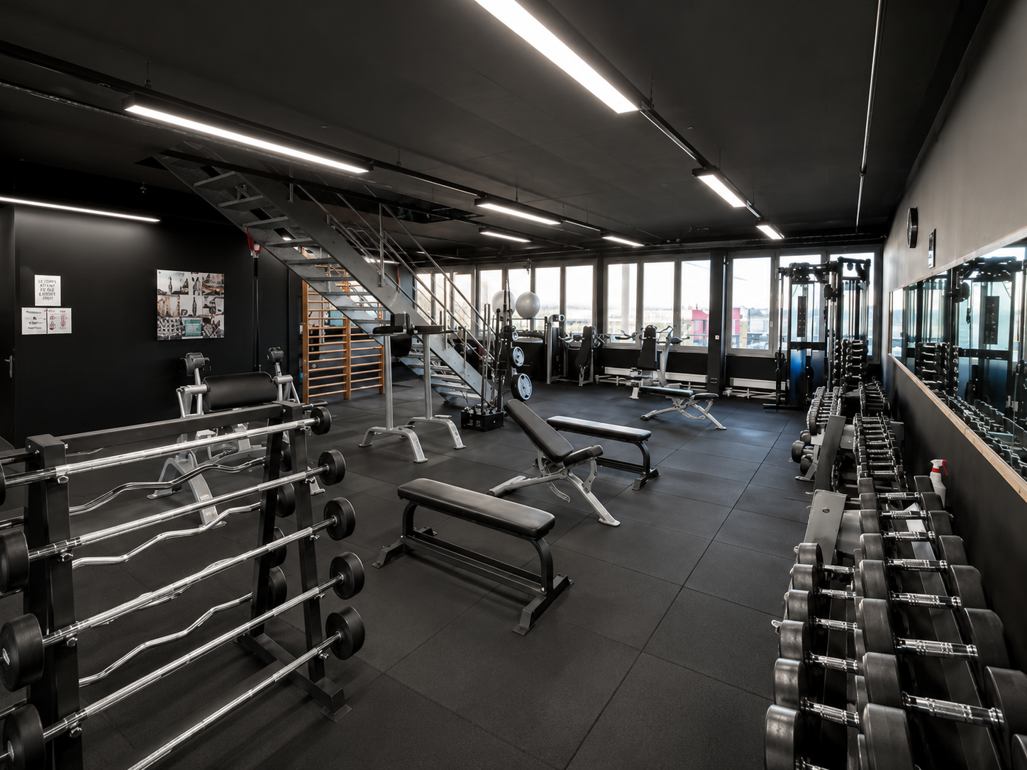 Intérieur de salle de sport moderne avec supports pour haltères, bancs et machines de musculation sur un sol en caoutchouc noir