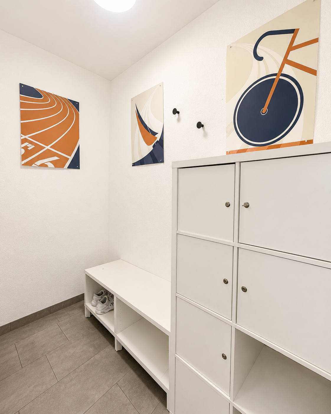 Pièce de rangement blanche avec casiers, banc et œuvre murale abstraite orange, bleue et noire.