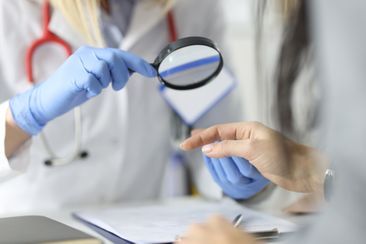 Ärztin schaut mit einer Lupe auf die Hand eines Patienten