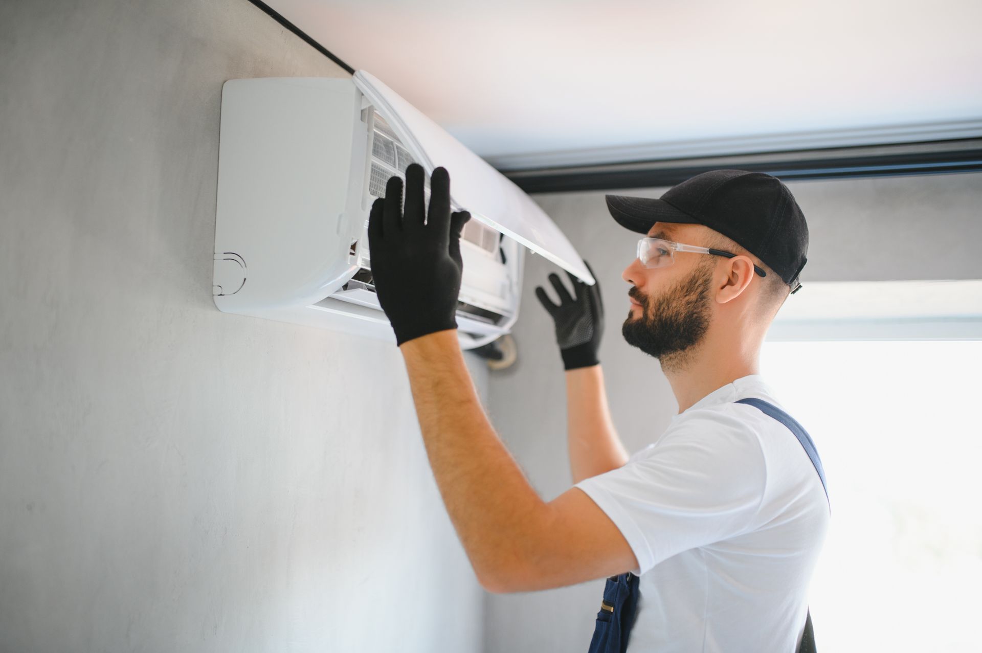 Des mains gantées nettoient un filtre blanc de grille d'aération au plafond.