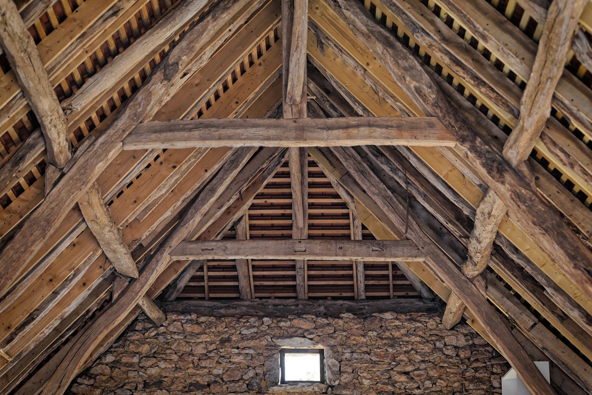 Poutres de toit en bois à l'intérieur d'un bâtiment en pierre, avec une petite fenêtre en bas.
