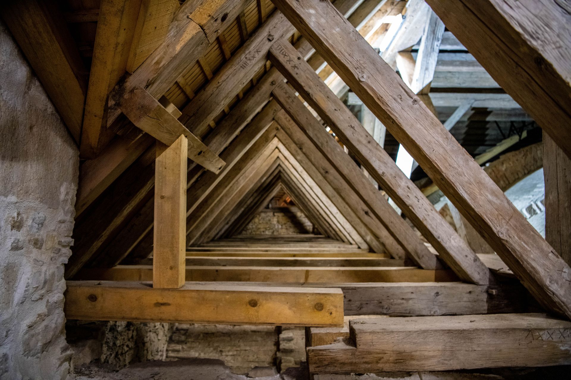 Vue intérieure d'une charpente en bois, avec des chevrons triangulaires convergeant vers l'horizon.
