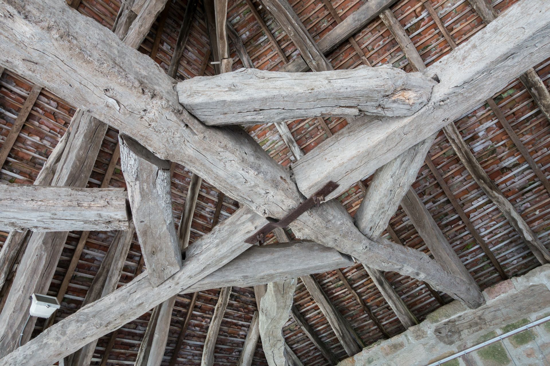 Poutres en bois formant la structure intérieure du toit d'un bâtiment ; toit de tuiles rouges visible en dessous.