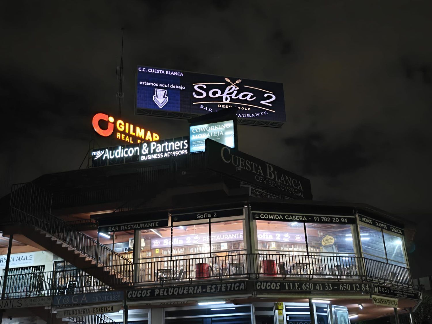 Vista nocturna de un edificio de varios niveles con carteles iluminados, incluidos 