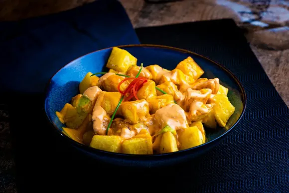 Tazón azul de curry de pollo con mango y guarnición de pimiento rojo.