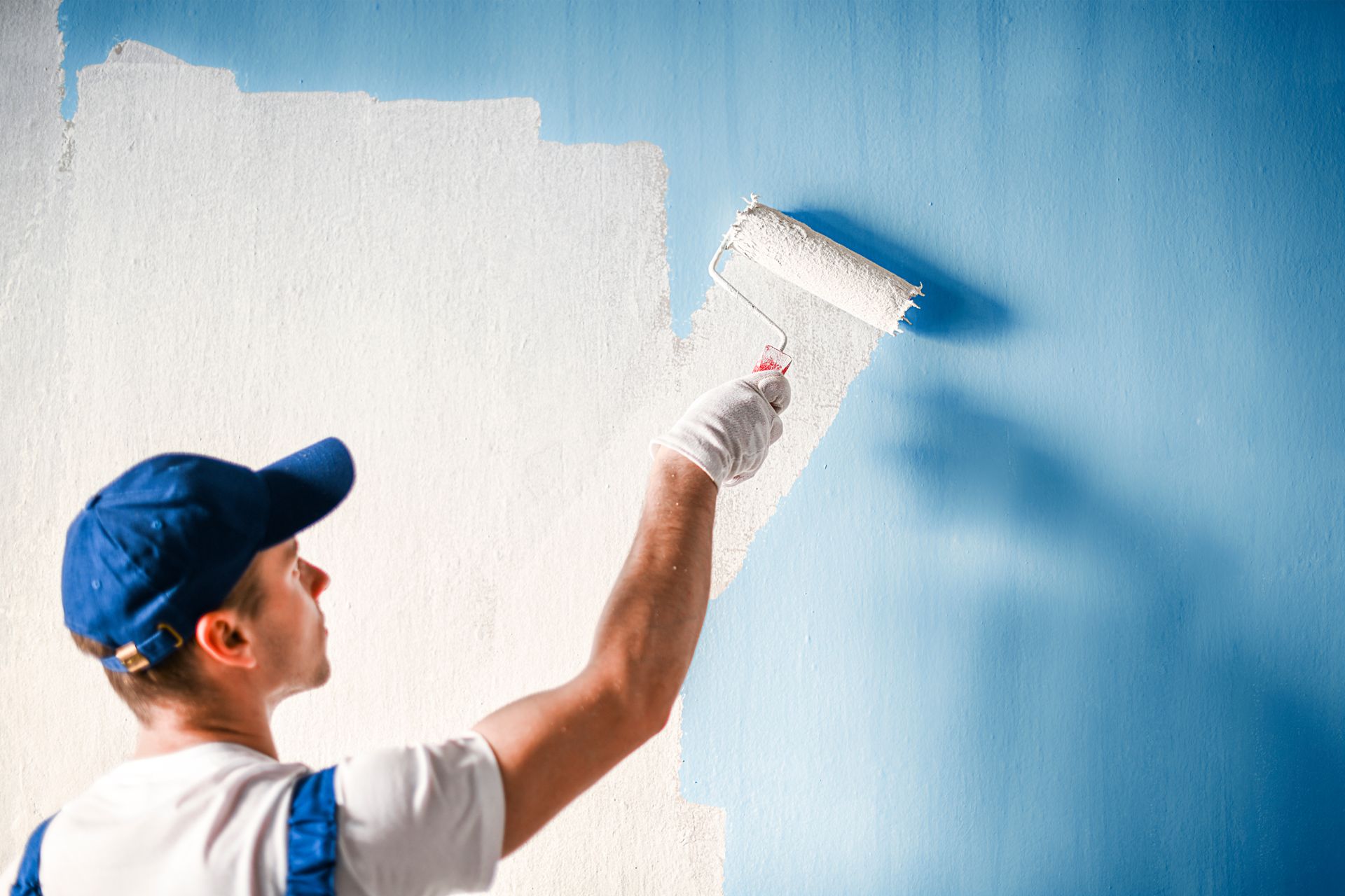 Peintre qui recouvre un mur bleu de peinture blanche